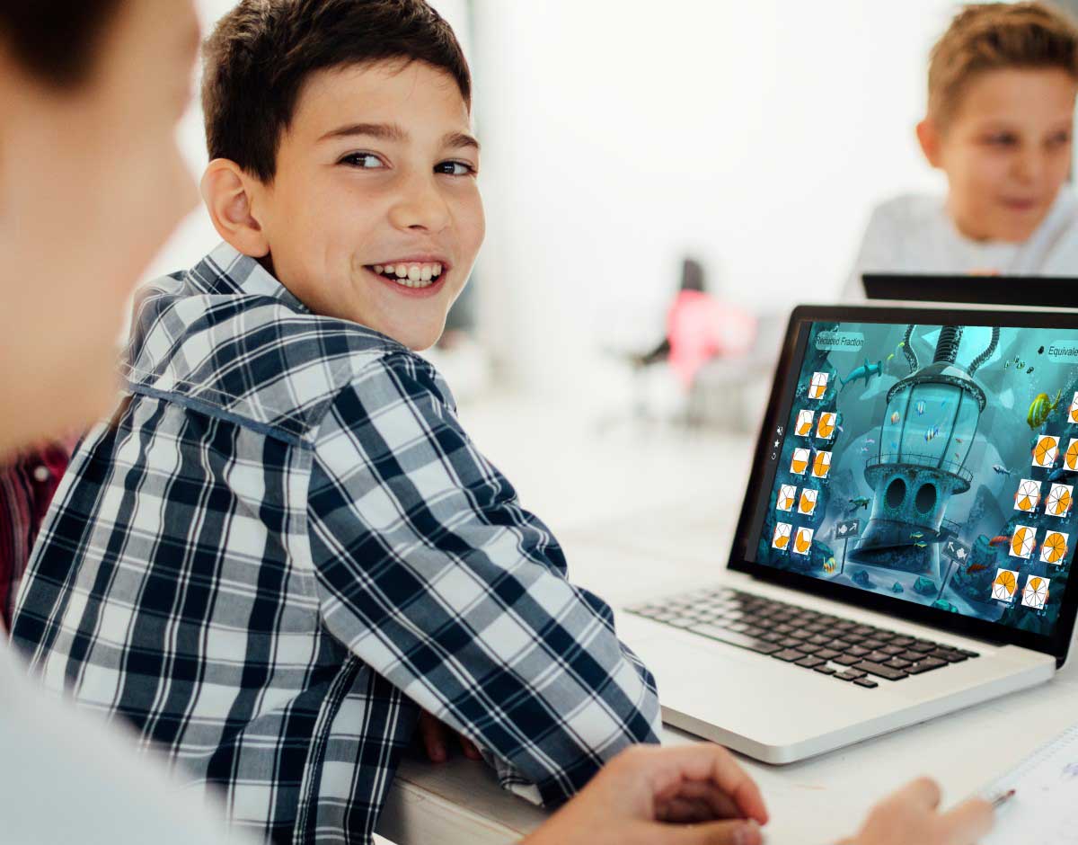 Smiling young boy in a classroom, looking back over his shoulder with a laptop displaying a Lumio activity on the screen.